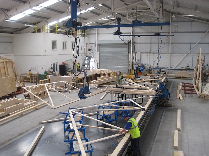 Wide view over the TrussGuy shop floor — truss lines on the jig, the overhead crane, and the full plant in Gaffney