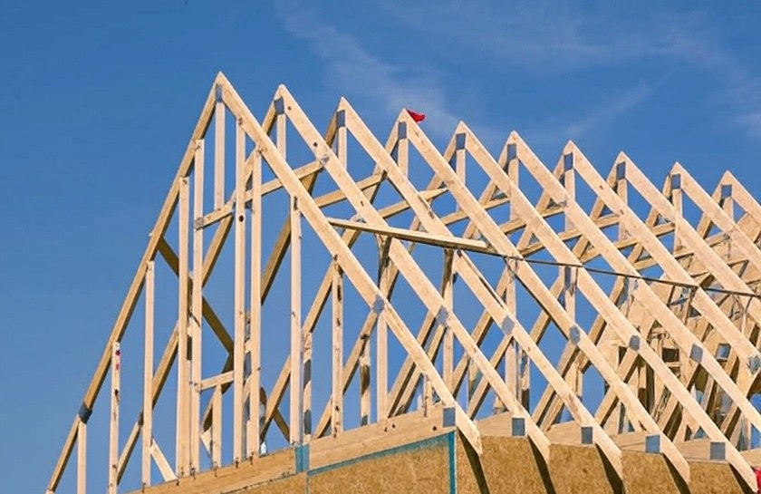 Wood roof trusses set in a row on a house under construction against a blue sky